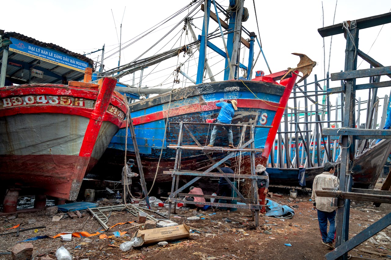 Workers repairing colorful fishing boats in a busy dockyard, focusing on teamwork and craftsmanship.