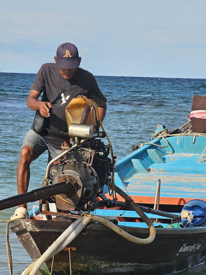 Man navigating a motorized boat in the ocean, performing maintenance.