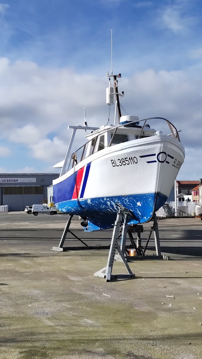 A boat stands elevated on a dry dock under a blue sky with clouds, emphasizing maintenance and maritime themes.